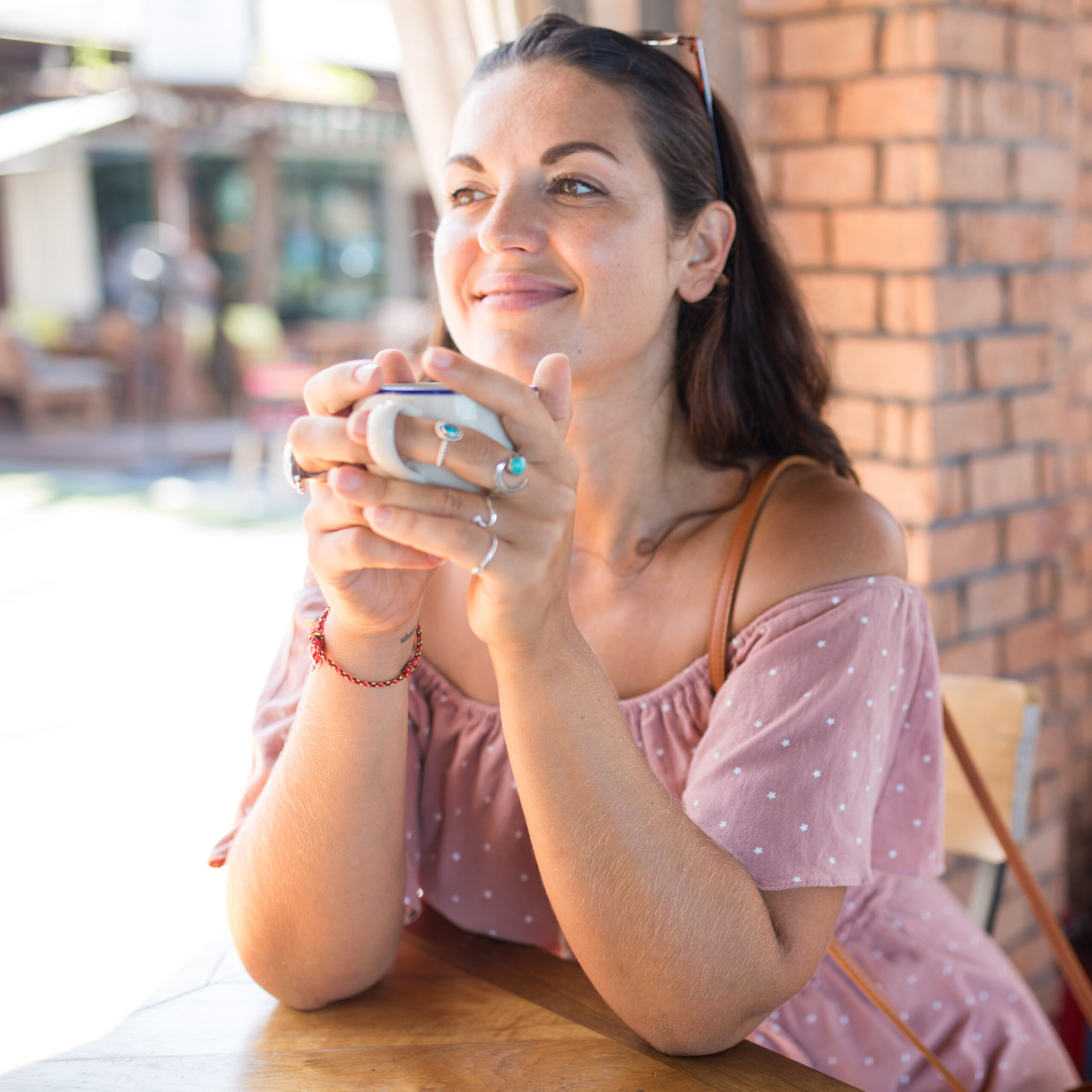 woman sitting in outdoor cafe drinking coffee and smiling