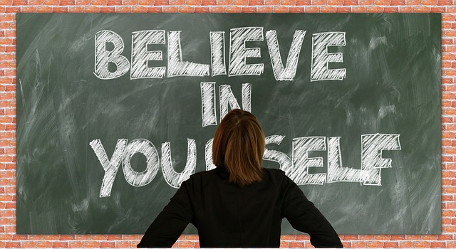 woman standing in front of chalkboard with the words Believe in yourself written on it