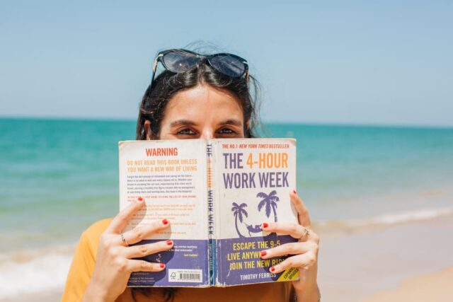 woman on the beach holding a copy of The 4-hour work week in front of her face